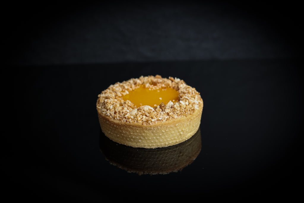 Small tart with a crumbly crust and yellow filling on a dark background