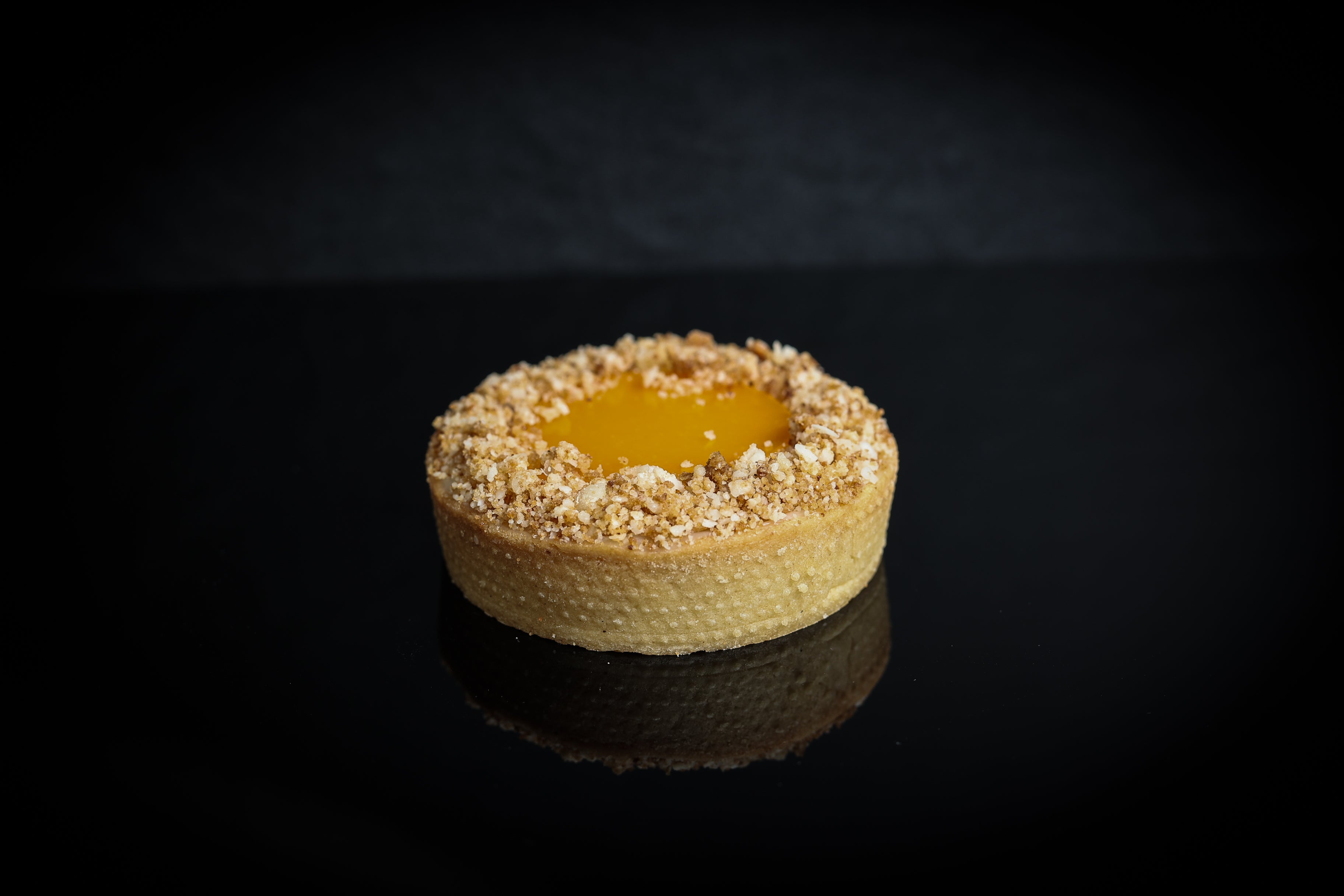Small tart with a crumbly crust and yellow filling on a dark background