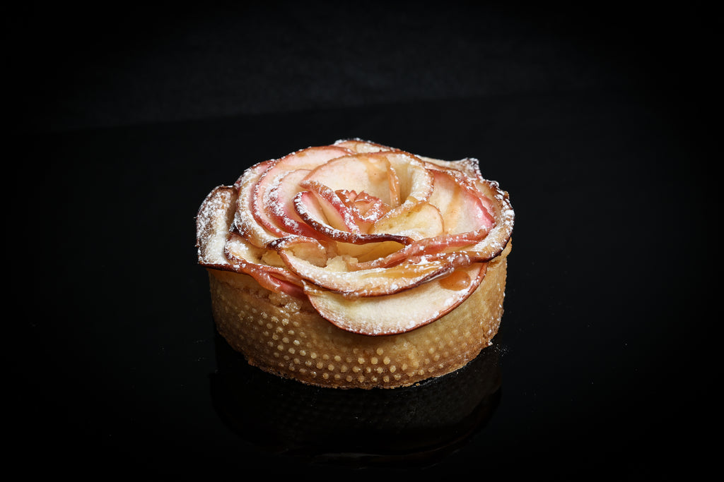 Apple tartlet with a rose-shaped apple garnish on a black background