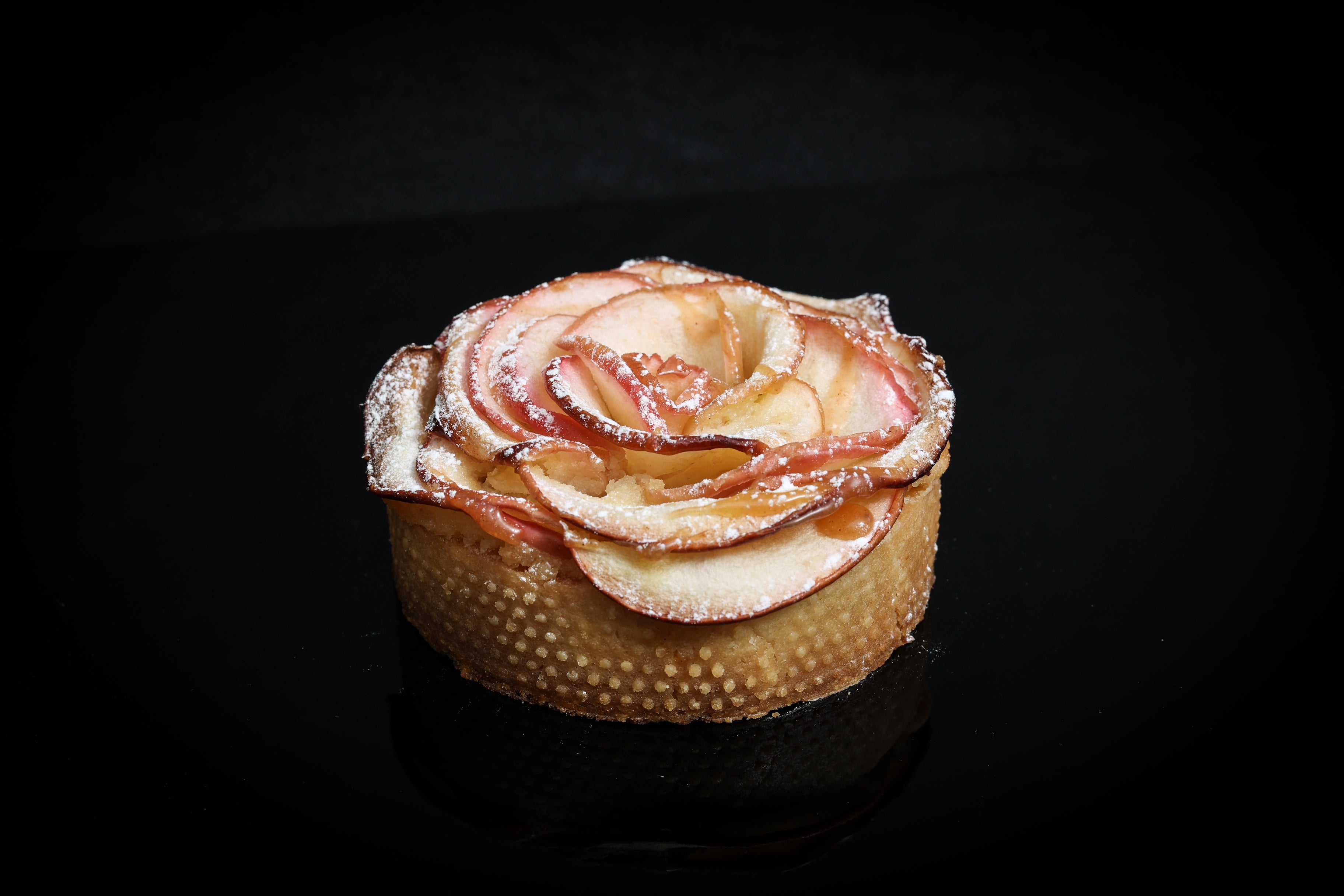 Apple tartlet with a rose-shaped apple garnish on a black background