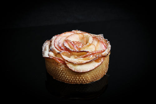 Apple tartlet with a rose-shaped apple garnish on a black background