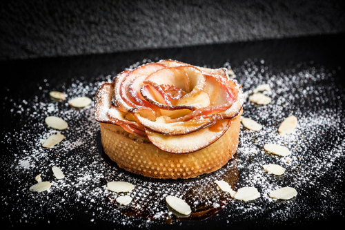Apple tart with a rose made of apples on a dark surface
