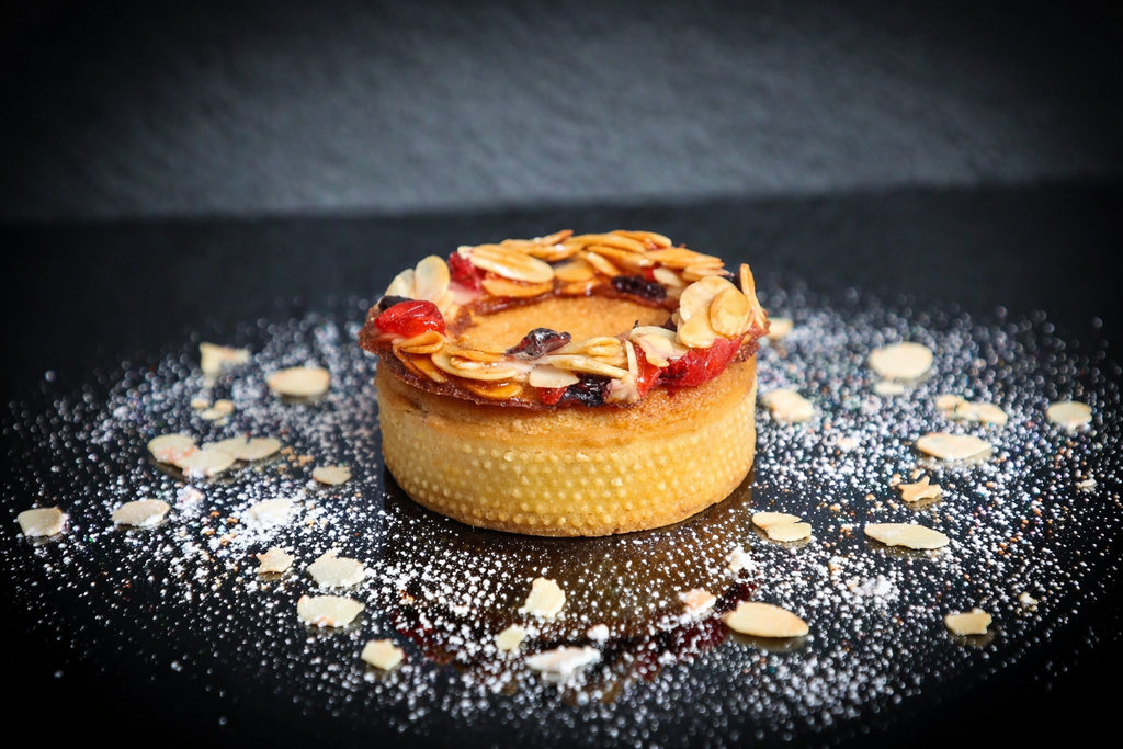 Small dessert tart with almonds and berries on a dark surface