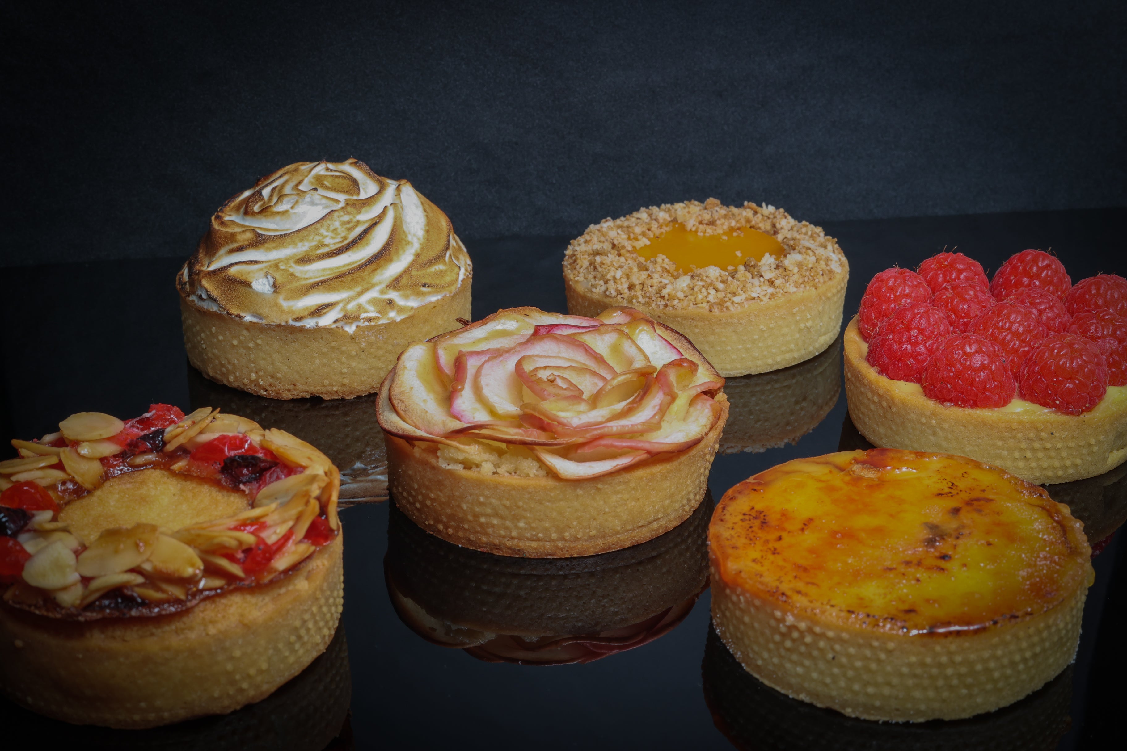 Assorted small pies with different toppings on a reflective surface