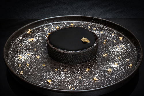 Black dessert on a black plate with gold flakes on a dark background