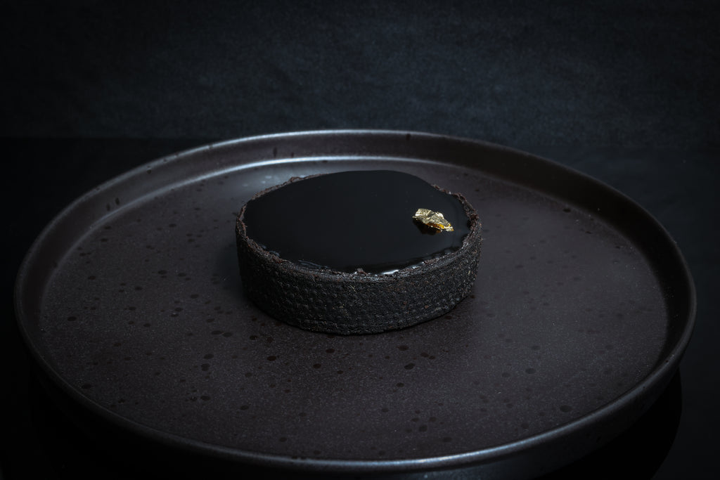 Dark chocolate tart on a black plate with a dark background