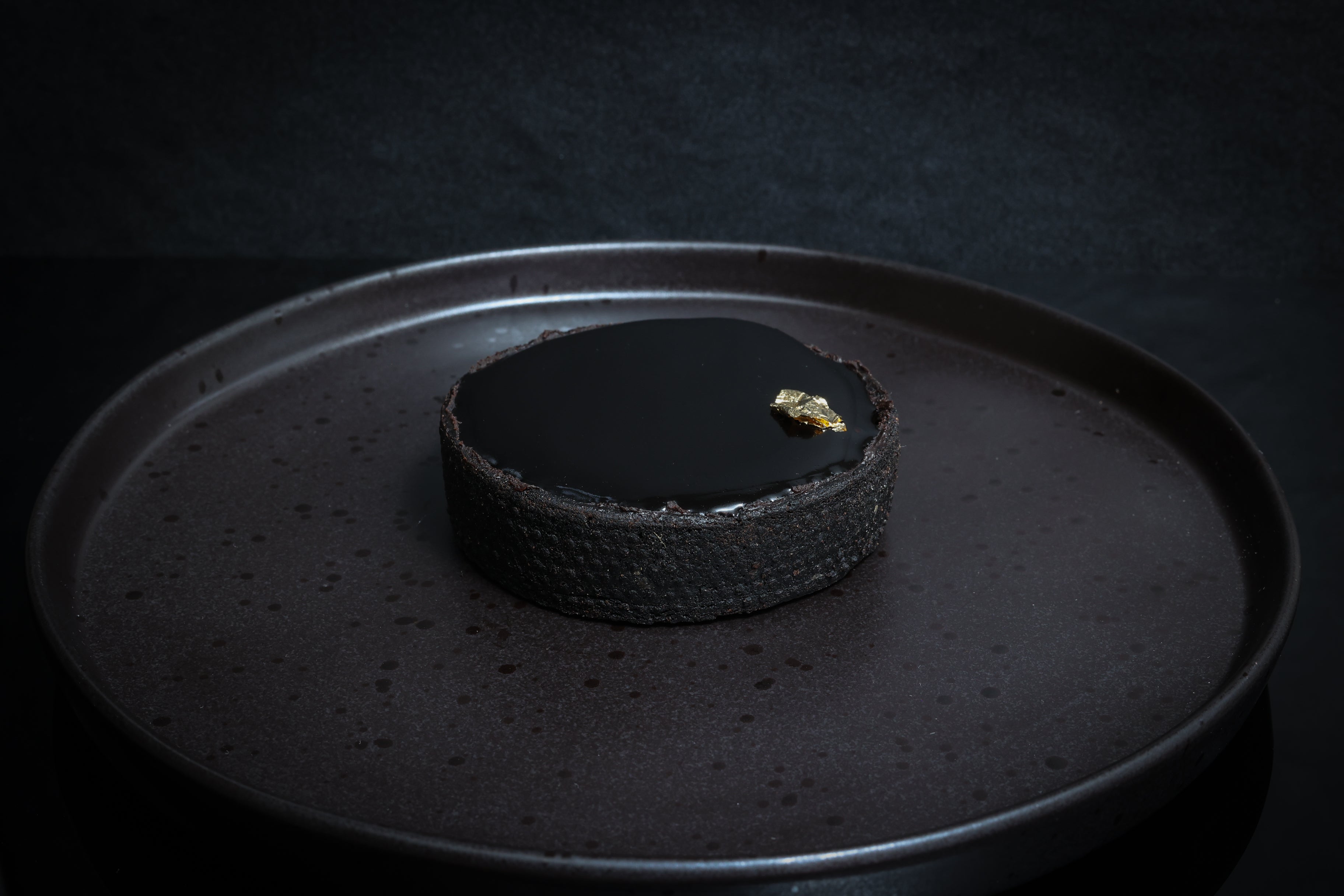 Dark chocolate tart on a black plate with a dark background