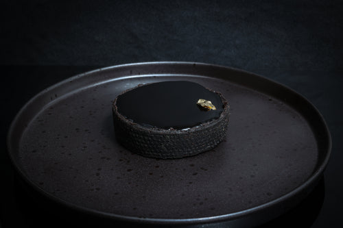 Dark chocolate tart on a black plate with a dark background