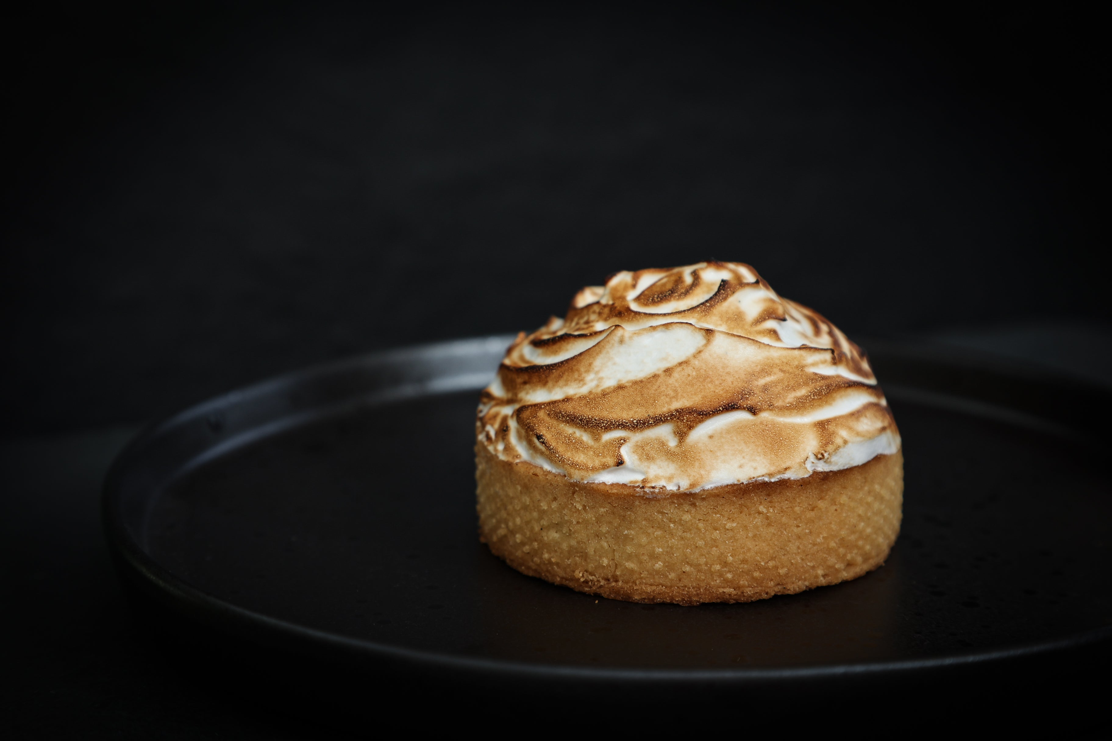 Small cake with meringue topping on a black plate against a dark background