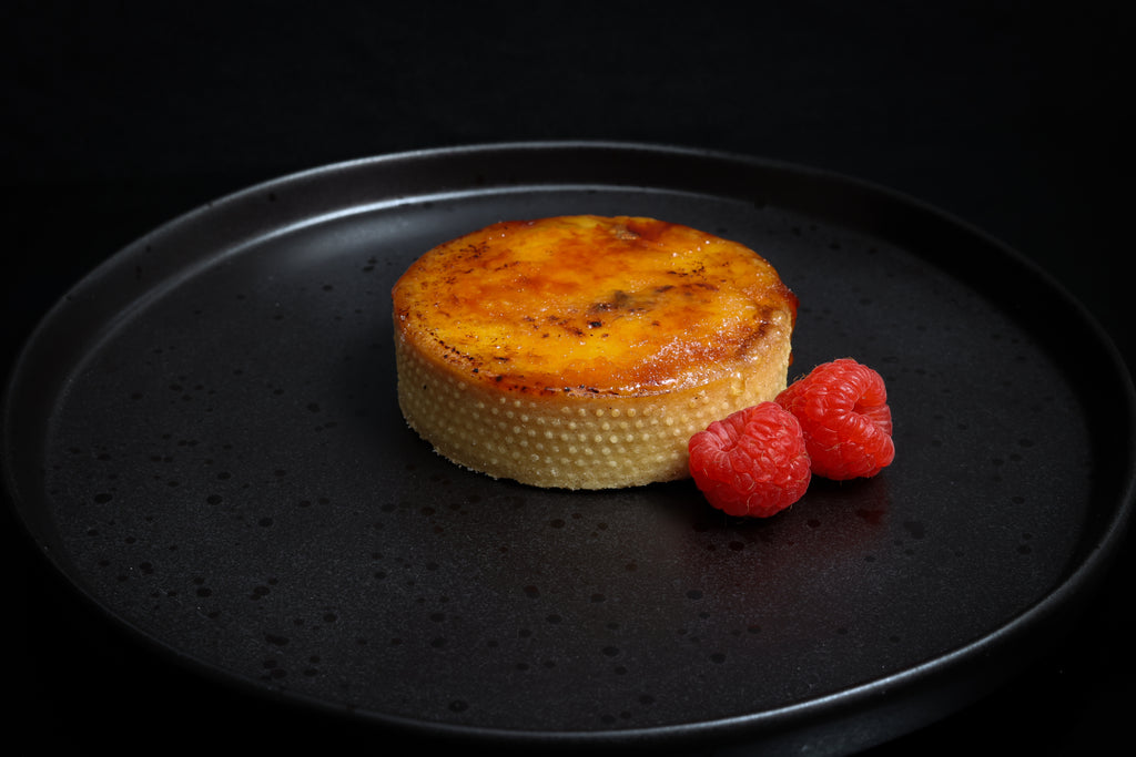 Round baked dish on a black plate with raspberries