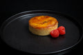 Round baked dish on a black plate with raspberries
