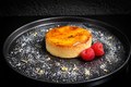 Custard tart with raspberries on a black plate