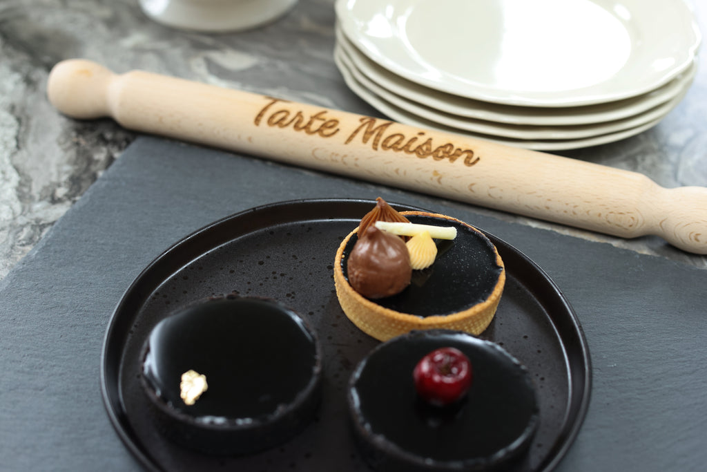 Dessert platter with small pastries and a rolling pin with 'Tarte Maison' branding on a gray surface.