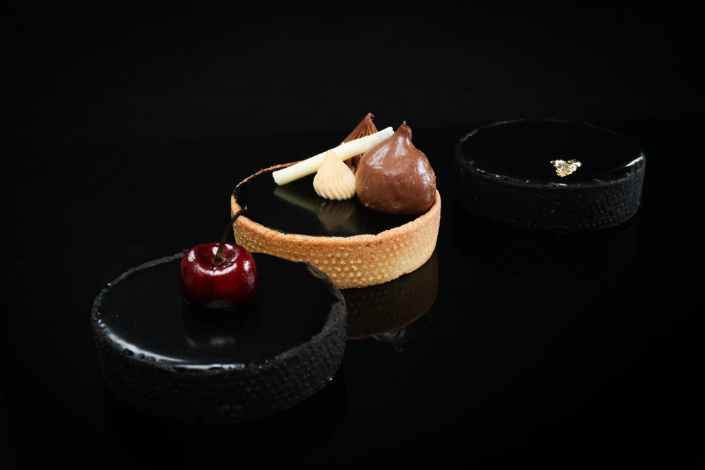 Delicate dessert with a tartlet, chocolate mousse, and cherry on a black background